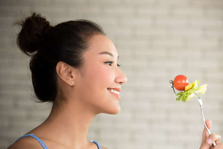 Asian woman in joyful postures with hand holding salad on forkの写真素材