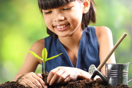 A girl planting young plant on soil with a hope of good environmentの写真素材