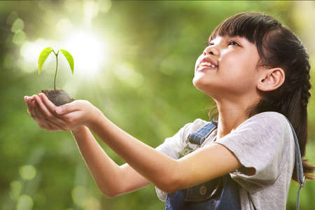 A girl holding a young plant in her hands with a hope of good environment