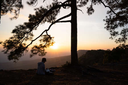 Image of sunrise or sunset on orange and yellow horizon with people's silhouette surrounded by pine trees ( Phu kradueng Thailand )の写真素材