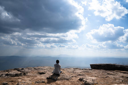 A person sitting  on rocky mountain looking out at scenic natural view and beautiful blue skyの写真素材