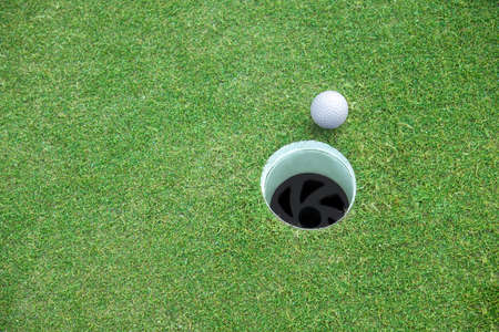 Golf ball and golf hole on green grass with copy space