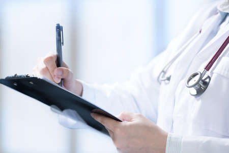 Medical doctor writing and taking notes on cliboard in hospital settingの写真素材
