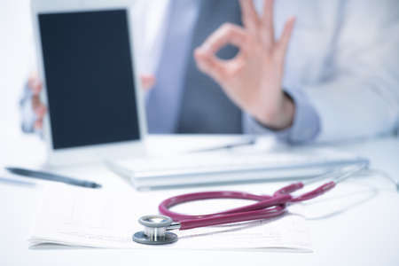 Medical doctor explaining to patient using tablet with stethoscope on the deskの写真素材