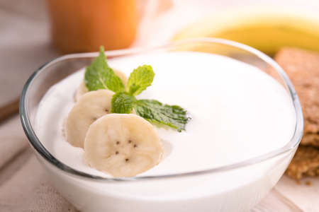Plain yogurt with fresh bananas on top in bowl on the tableの写真素材
