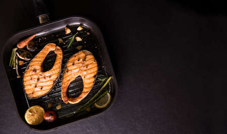 Grilled salmon fish with various vegetables on pan on black stoneの写真素材
