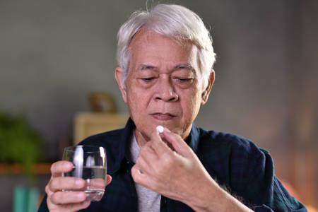 Asian senior man taking pills at homeの写真素材