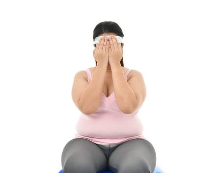 Overweight Asian woman sitting on a gym ball looking stressed covers her face with her hands isolated on white backgroundの写真素材