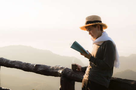 Asian middle aged woman standing and reading book at beaitiful natural viewの写真素材