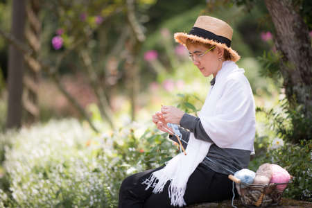 Middle aged Asian woman sitting on the bench and knitting for winter Christmas at beaitiful natural viewの写真素材