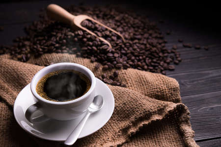 Cup of coffee with smoke and coffee beans on old wooden