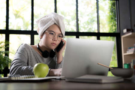 Asian young woman in casual clothing using laptop and smiling while working from homeの写真素材