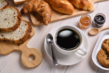 Top view of cup of coffee with breads or bun, croissant and bakery on white wooden tableの写真素材