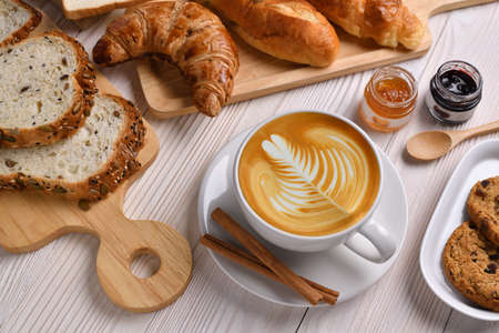 Top view of cup of coffee latte with breads or bun, croissant and bakery on white wooden tableの写真素材