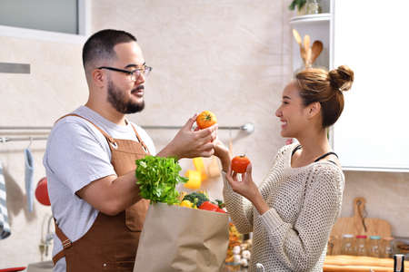 Loving young Asian couple using digital tablet and cooking in kitchen making healthy food together feeling funの写真素材