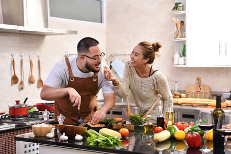 Loving young Asian couple using digital tablet and cooking in kitchen making healthy food together feeling funの写真素材