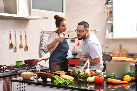 Loving young Asian couple using digital tablet and cooking in kitchen making healthy food together feeling funの写真素材