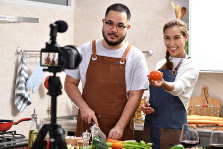 Young Asian couple blogger vlogger and online influencer recording video content on healthy food in the kitchenの写真素材