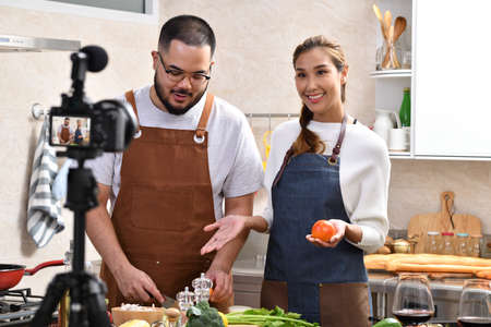 Young Asian couple blogger vlogger and online influencer recording video content on healthy food in the kitchenの写真素材