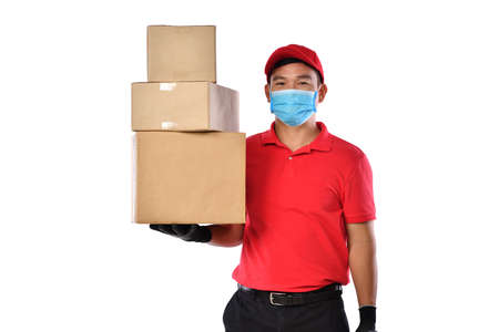 Happy young Asian delivery man in red uniform, medical face mask, protective gloves carry cardboard...