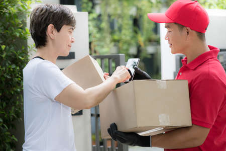 Asian delivery man in red uniform delivering parcel box to woman recipient at home with recipient...