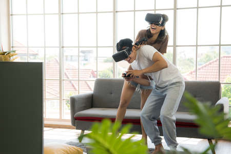 Young happy Asian couple playing video games wearing virtual reality glasses in their apartmentの写真素材