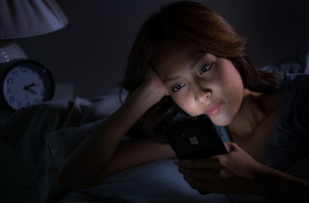 Young woman using a smartphone in her bed at nightの写真素材