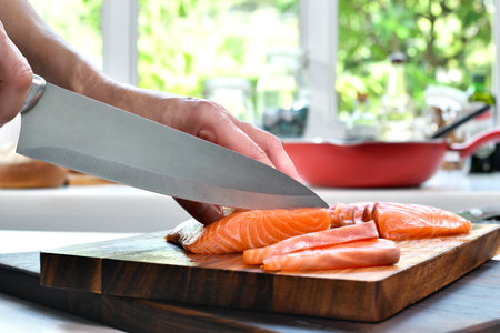 Hand slicing fresh raw salmon fillet steaks on a cutting board in the kitchenの写真素材