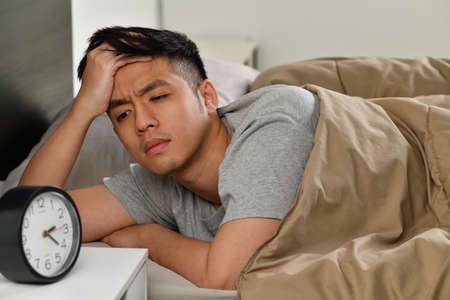 Depressed young Asian man lying in bed cannot sleep from insomniaの写真素材