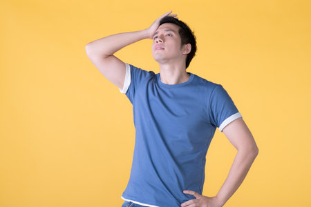 Asian man is bored, isolated on yellow backgroundの写真素材