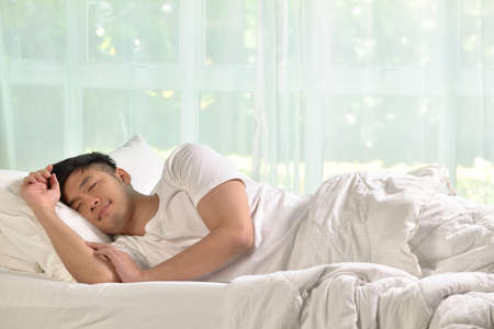 Young Asian man sleeping in bedの写真素材