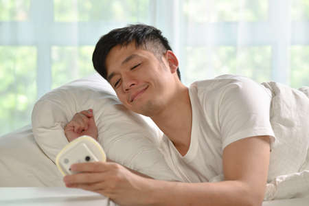 Portrait of happy Asian man waking up in bed in the morningの写真素材