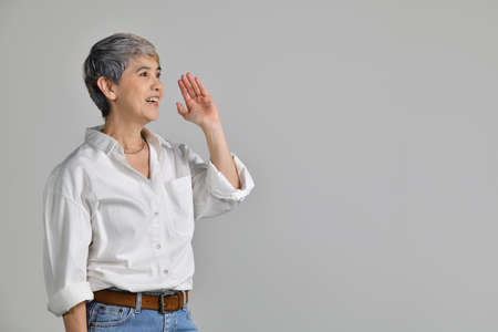 Middle aged Asian woman is holding hand near mouth and telling a secret isolated on white backgroundの写真素材