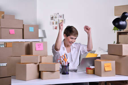 Successful middle aged Asian woman entrepreneur, Business owner with arms up while looking at laptop...
