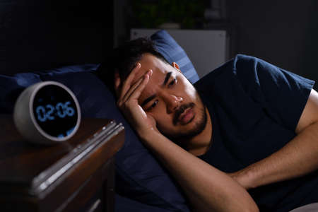 Depressed young Asian man lying in bed cannot sleep from insomniaの写真素材