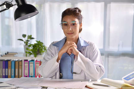 Portrait of young beautiful Asian female doctor looking at camera in medical office, having online consultation with patient. Young female doctor with stethoscope making video callの写真素材