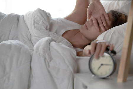 Woman turning off alarm clock in bedroom in the morning