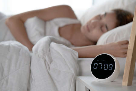 Young woman continues to sleep after turning off alarm clock in morning. focus on clockの写真素材