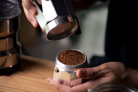 Barista holding moka pot with ground coffee in coffee shop.