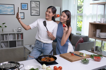 Young Asian lesbian couple looking happy while cooking and taking selfie. LGBT couple preparing meal...
