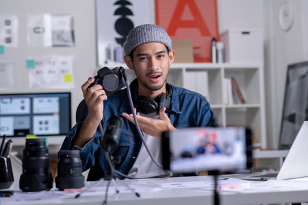 Young Asian man graphic designer blogger influencer filming teaching camera tutorial while looking at camera shooting education tutorial vlog training filming video course for social media at studio.の写真素材