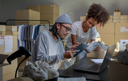 Mixed race couple of Asian man and African-American woman online seller confirming orders from customer on laptop and tablet computer.の写真素材