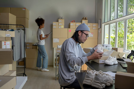 Mixed race couple of Asian man and African-American woman online seller e-commerce business owner working together in store warehouse.の写真素材