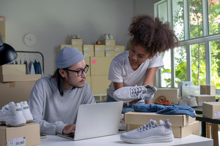 Mixed race couple of Asian man and African-American woman online seller confirming orders from customer on laptop computer.の写真素材