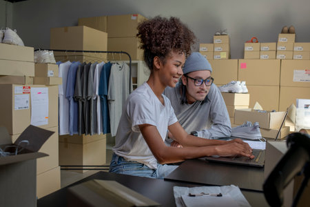 Mixed race couple of Asian man and African-American woman online seller confirming orders from customer on laptop.の写真素材