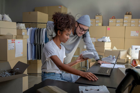 Mixed race couple of Asian man and African-American woman online seller confirming orders from customer on laptop.の写真素材