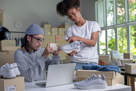 Mixed race couple of Asian man and African-American woman online seller confirming orders from customer on laptop computer.の写真素材