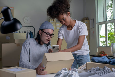 Mixed race couple of Asian man and African-American woman online seller using mobile app on smartphone checking parcel box.の写真素材