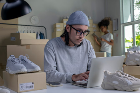 Mixed race couple of Asian man and African-American woman online seller confirming orders from customer on laptop computer.の写真素材
