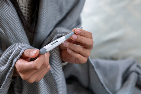 Closeup shot of a woman looking at thermometer. Female hands holding a digital thermometer. Girl measures the temperature.の写真素材
